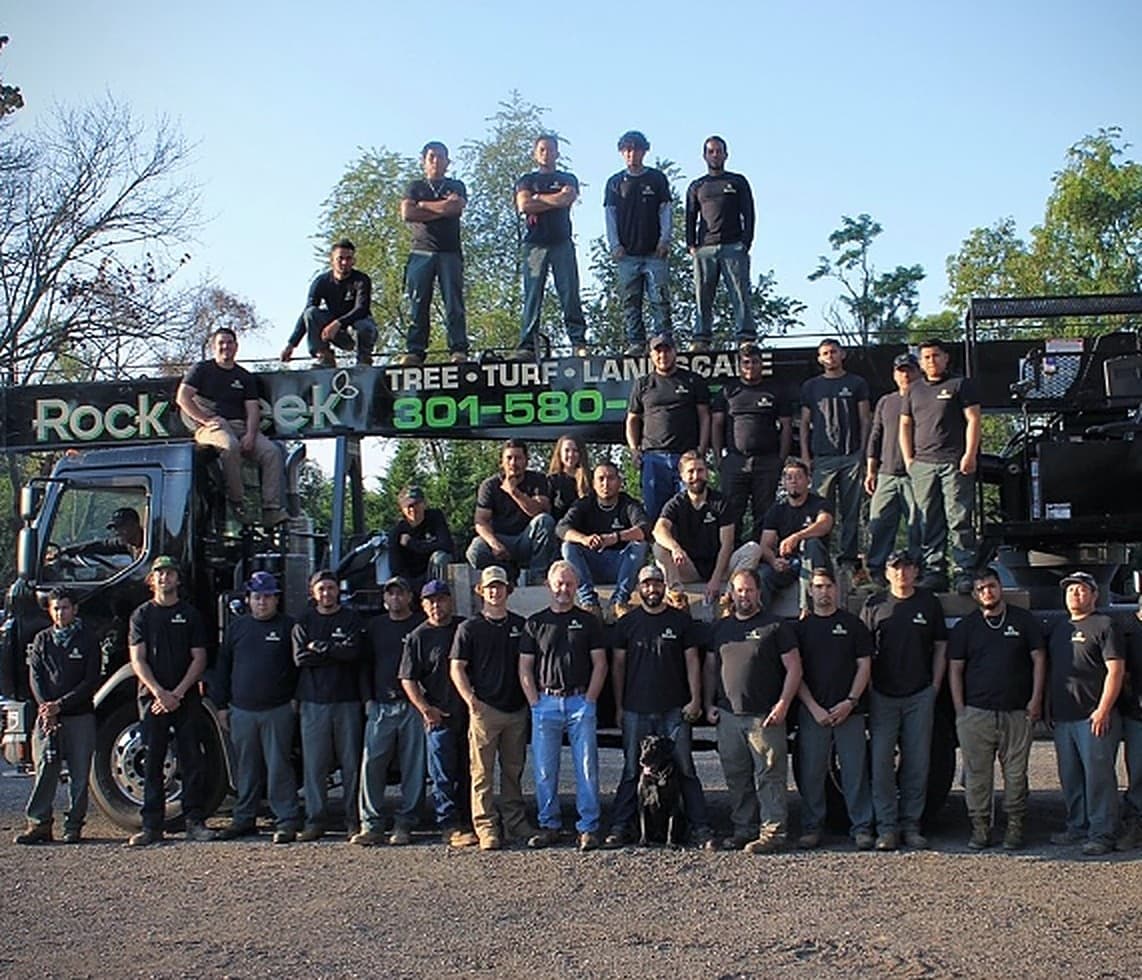 The full Rock Creek Tree, Turf & Landscape crew standing together with their branded company truck in Rockville, Maryland
