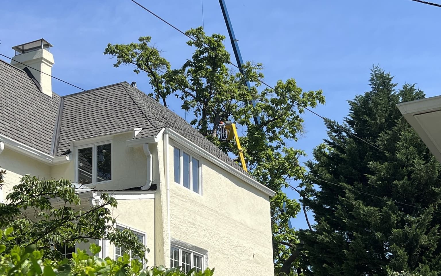A crane boom and the spider lift working above the roofline of a house, with overhead utility lines crossing the space between them