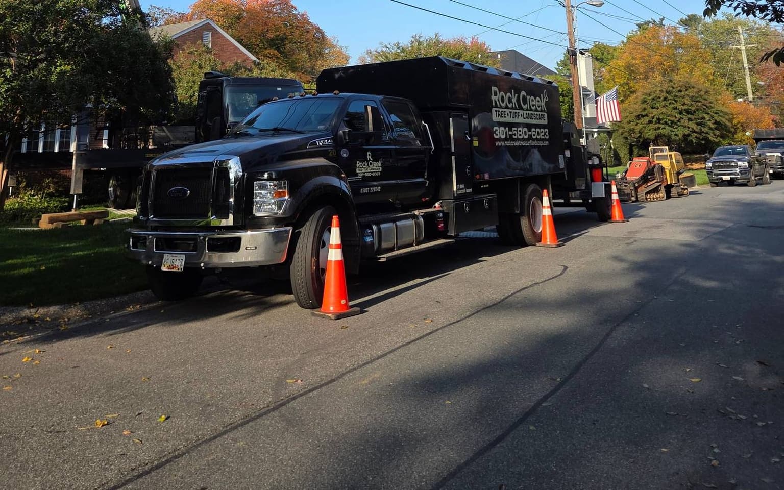 The Rock Creek chip truck parked along the street behind traffic cones, with the crane’s boom visible above the trees to the left